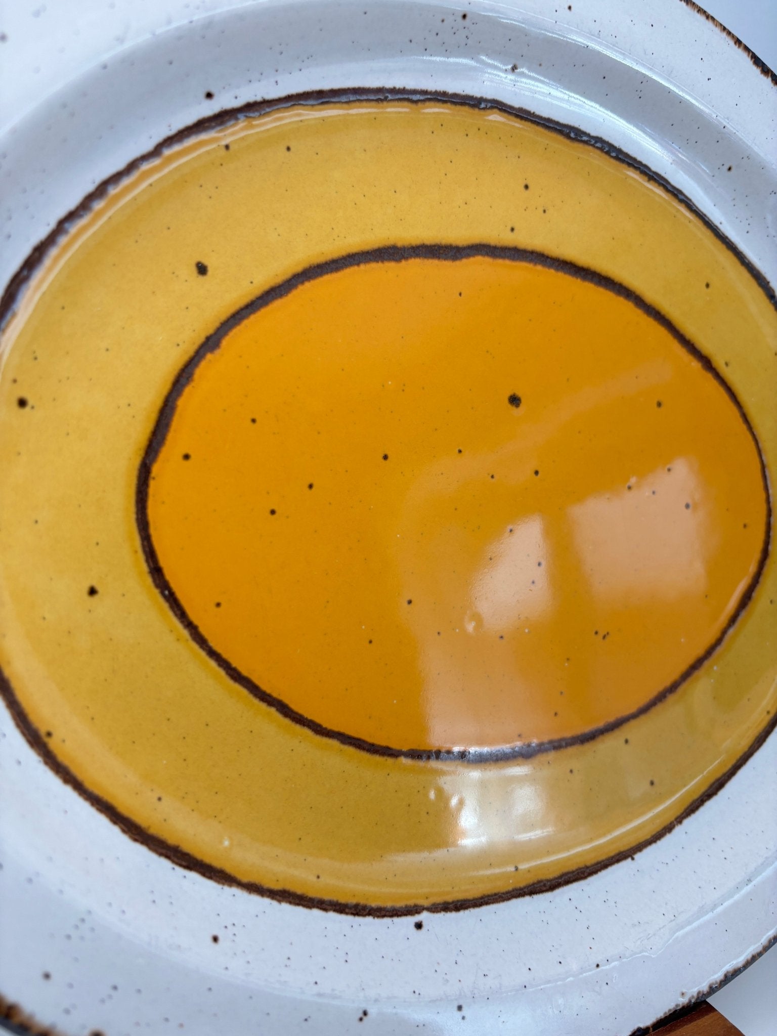 Yellow ceramic plate with brown rim on a white speckled surface
