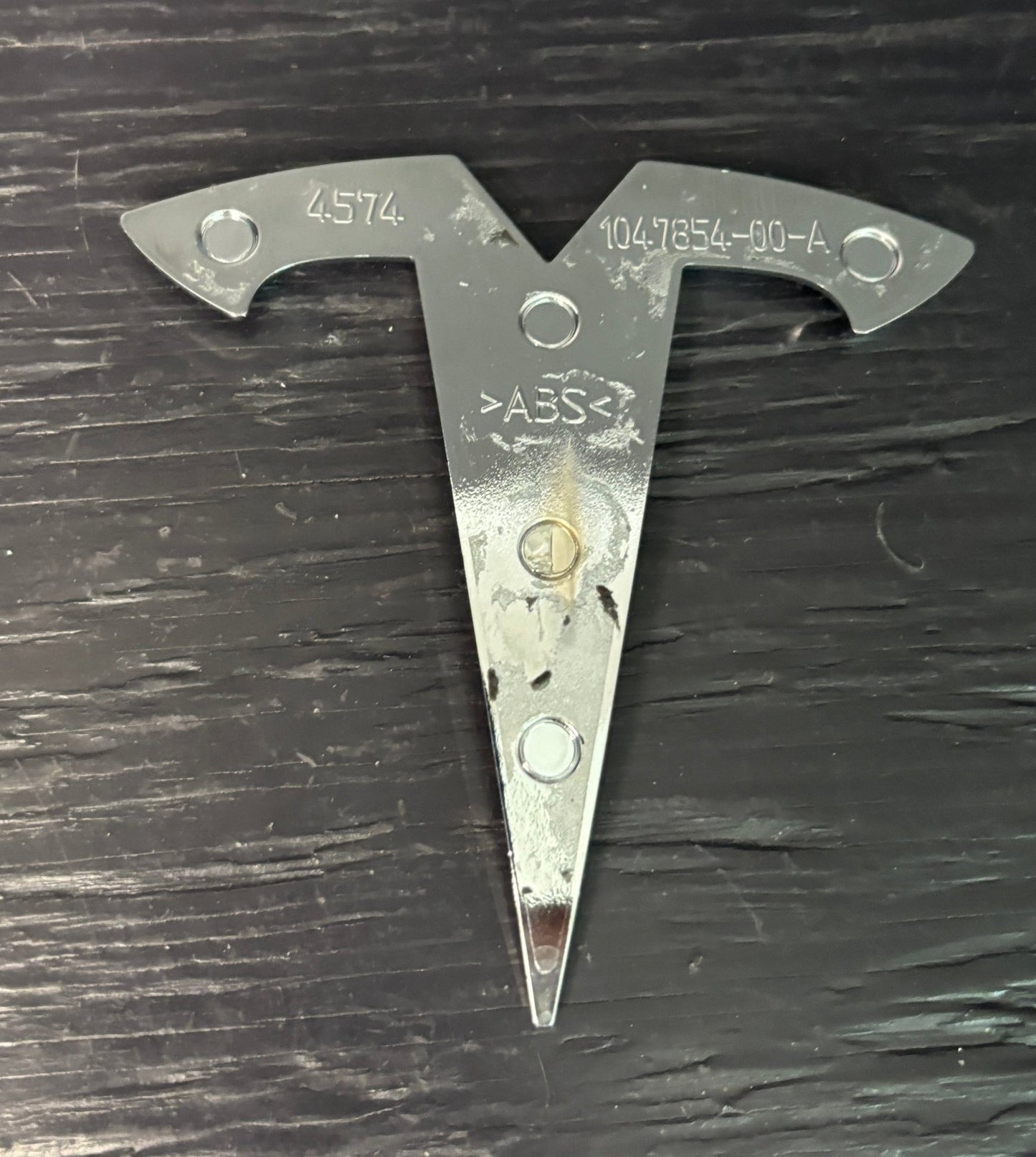 Metal triangular tool with 'ABS' marking on a dark surface