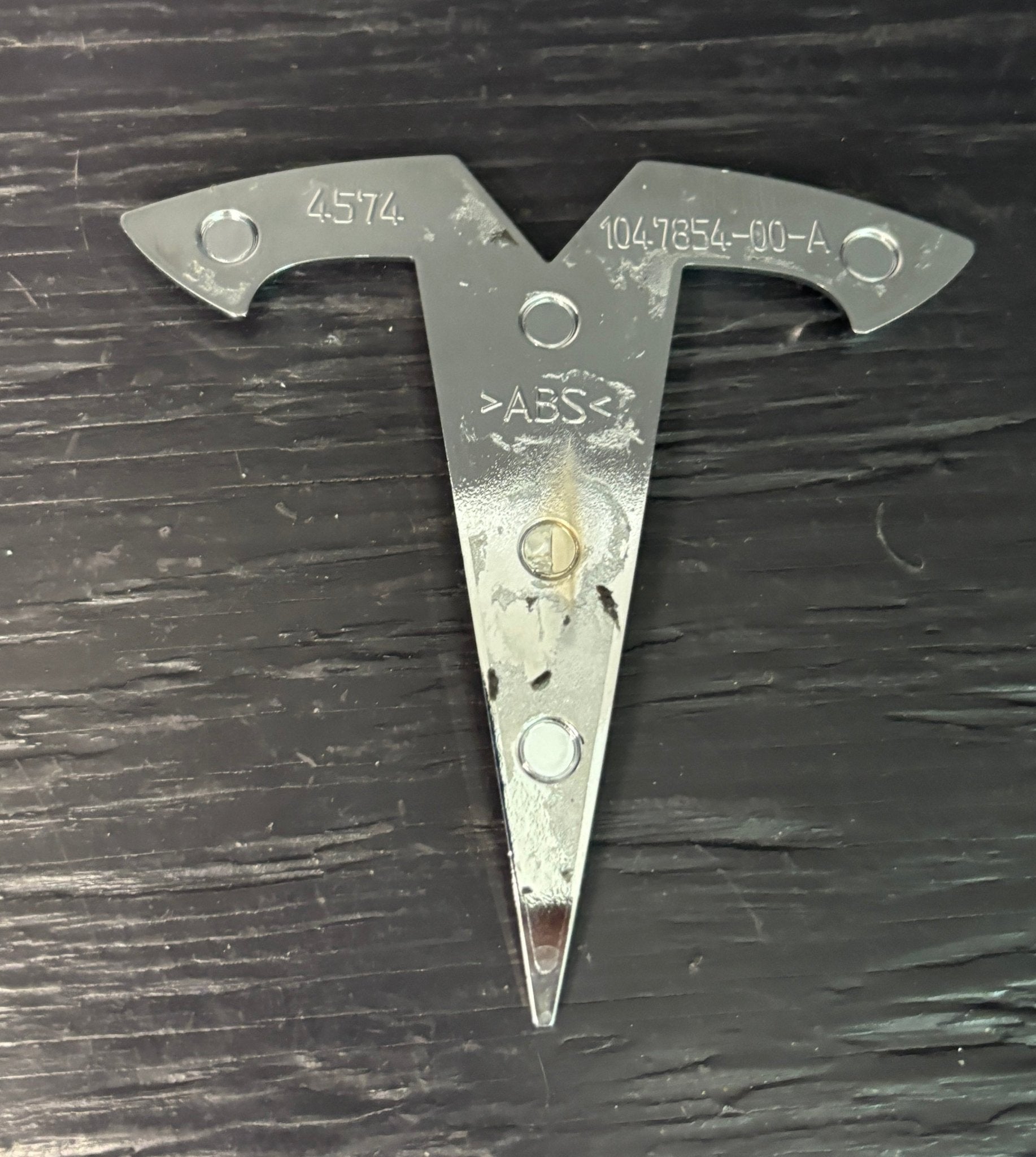 Metal triangular tool with 'ABS' marking on a dark surface