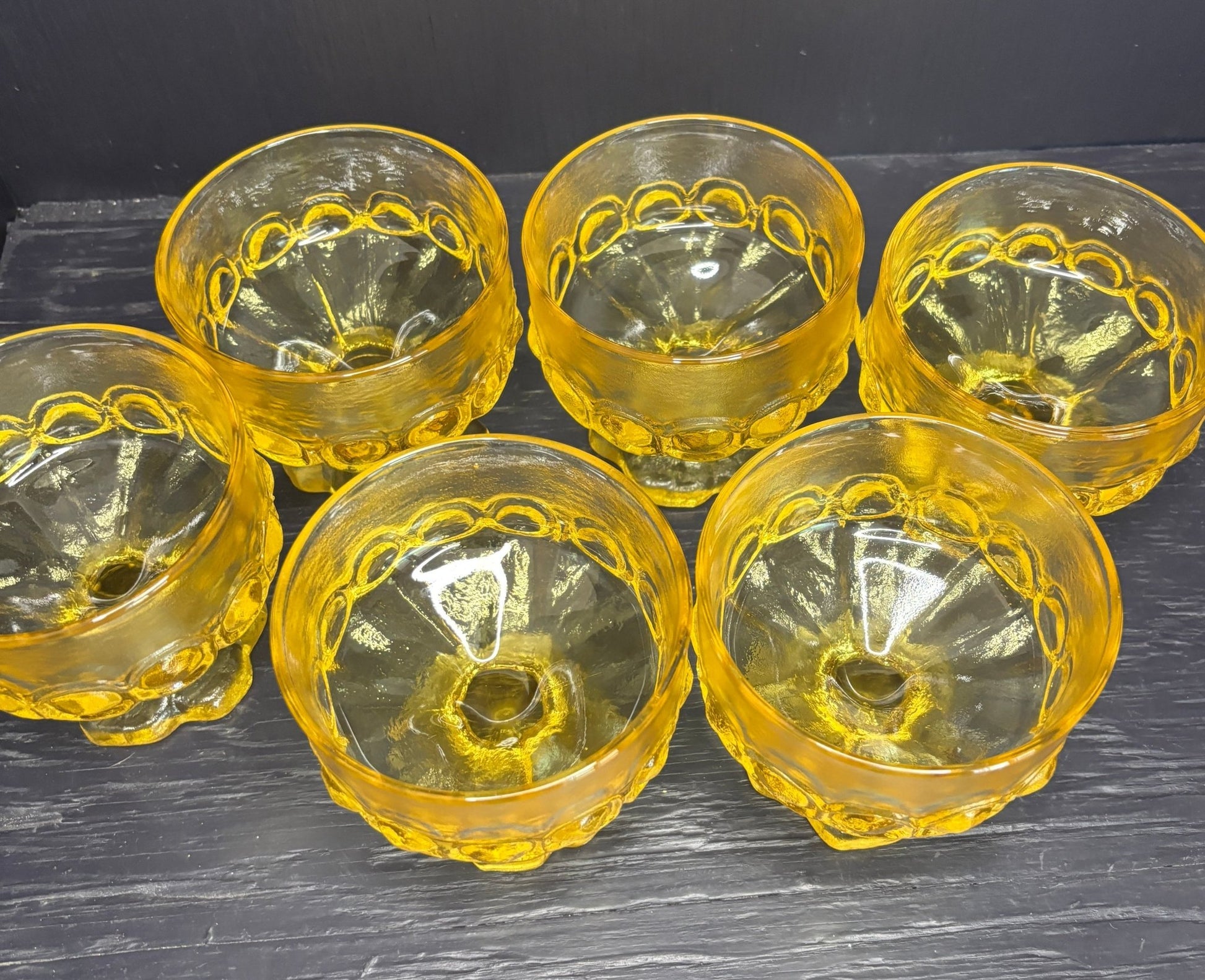 Set of six yellow glass bowls with decorative patterns on a dark surface