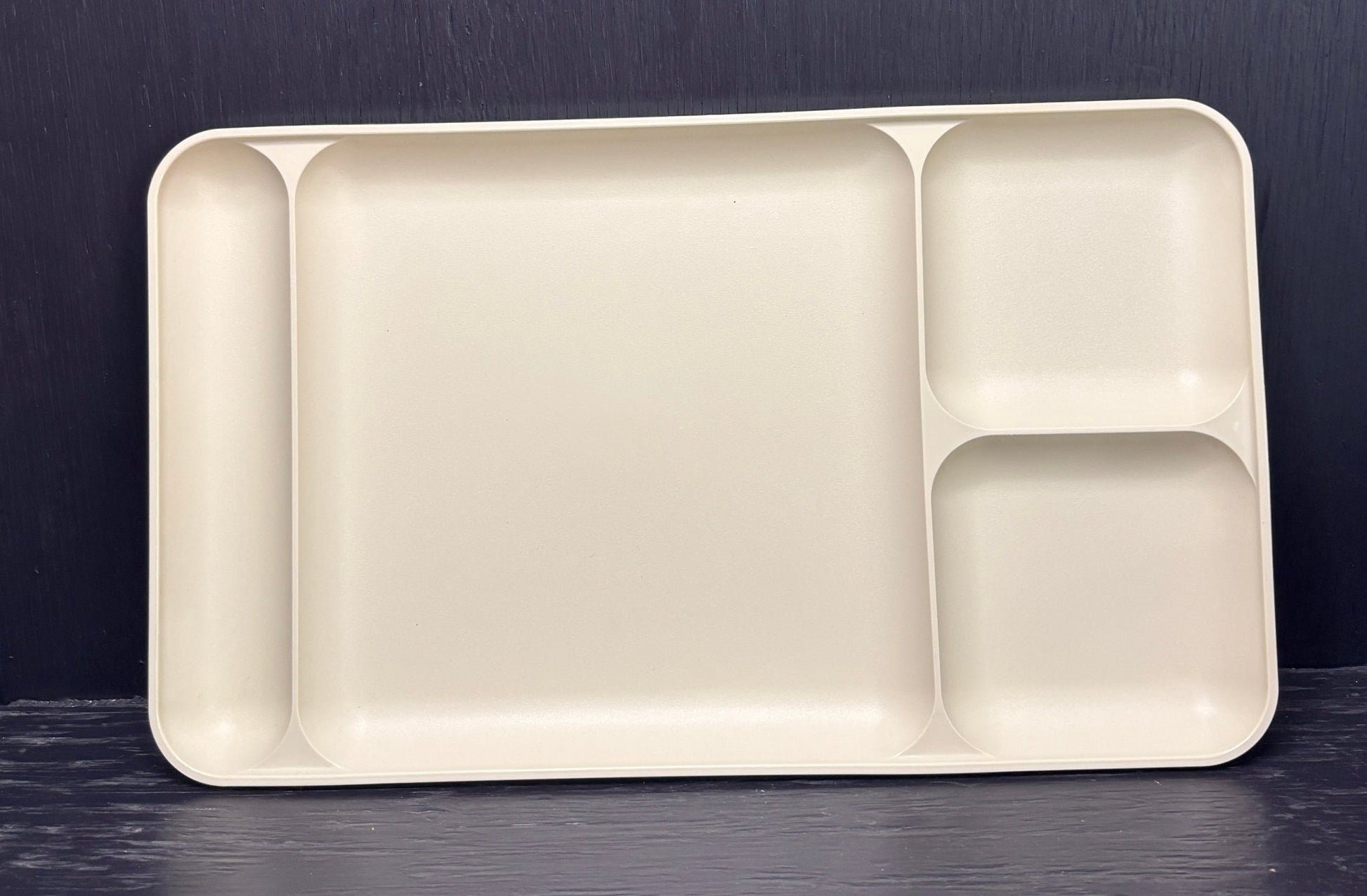 Beige plastic tray with compartments on a dark surface